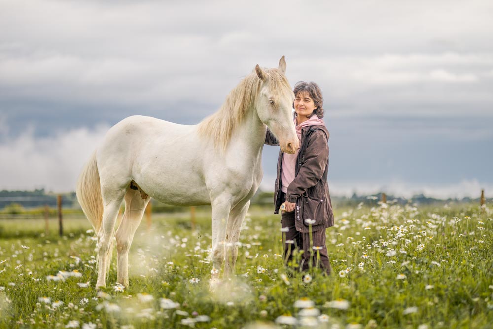 Cheval et sa propriétaire debout dans un pré de fleurs blanches