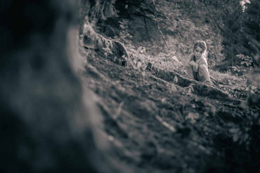 Enfant accroupie en forêt, l'enfant est dans un rayon de lumière alors que le reste de la forêt est plus sombre