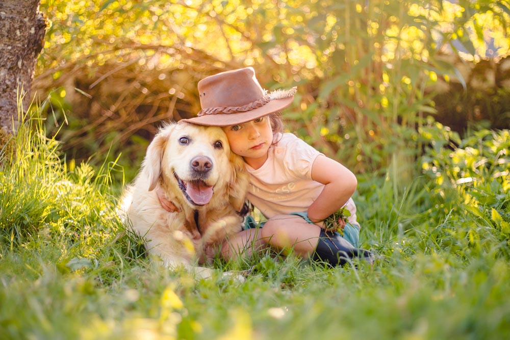 Enfant avec un chapeau assise avec son chien couché à côté d'elle, sa tête repose sur la tête de son chien