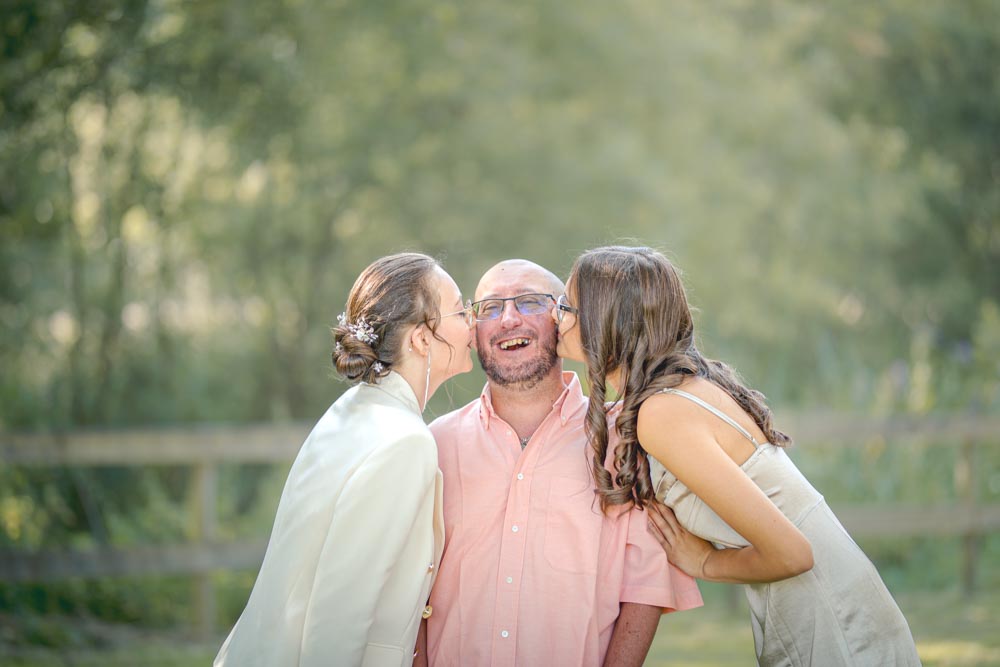 Un papa riant aux éclats avec ses deux filles lui embrassant les joues