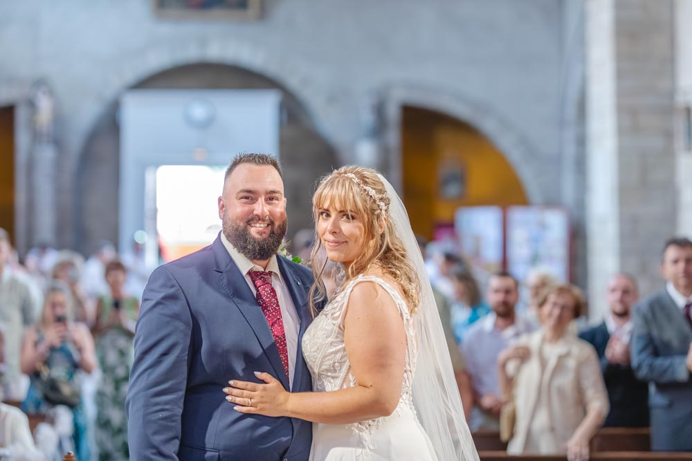 Couple souriant en fin de cérémonie religieuse, avec les invités qui applaudissent en arrière plan