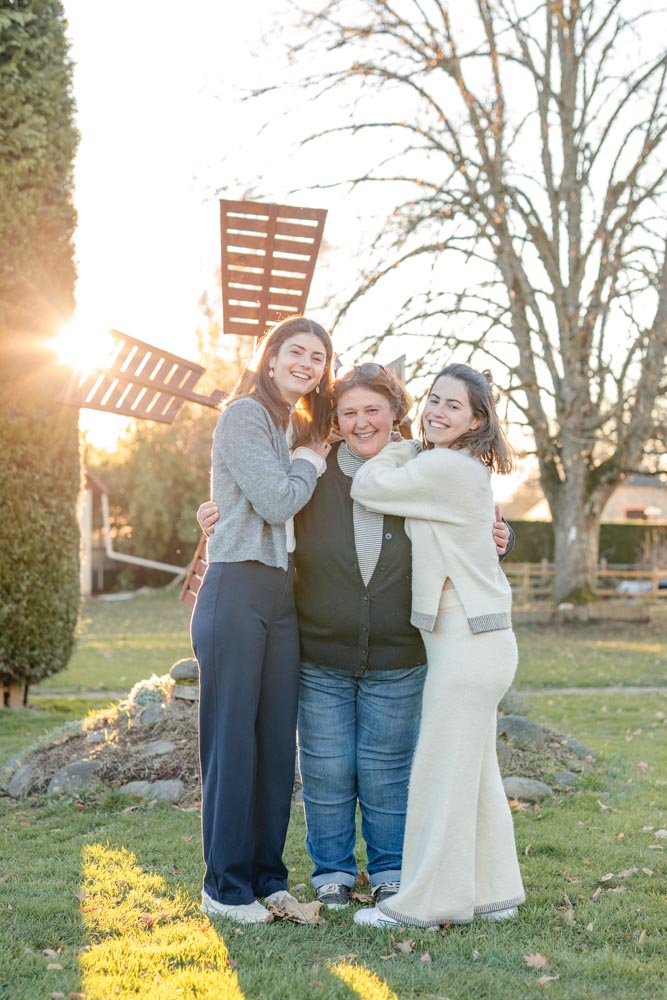 Mère et ses deux filles posant dans le jardin familial au coucher de soleil, toutes sont collées les unes aux autres et riant