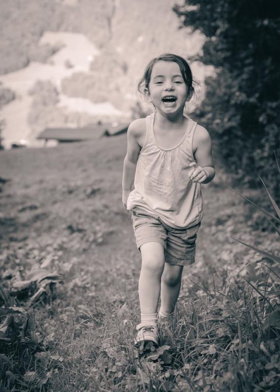 Photographie noir et blanc d'une enfant riant et courant vers le photographe