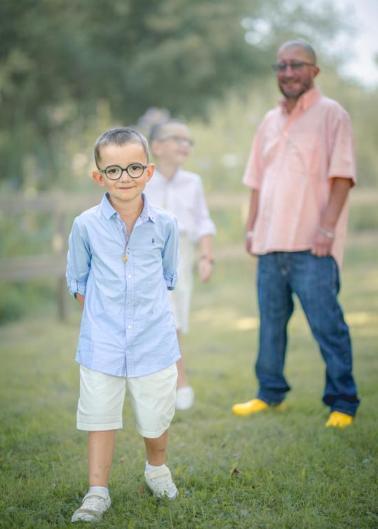 Enfant debout au devant de son frère et son père dans un parc verdoyant