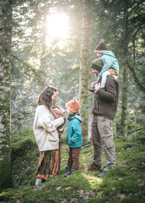 Photographie de famille en forêt, debout les pieds dans la mousse et la tête dans un rayon de soleil