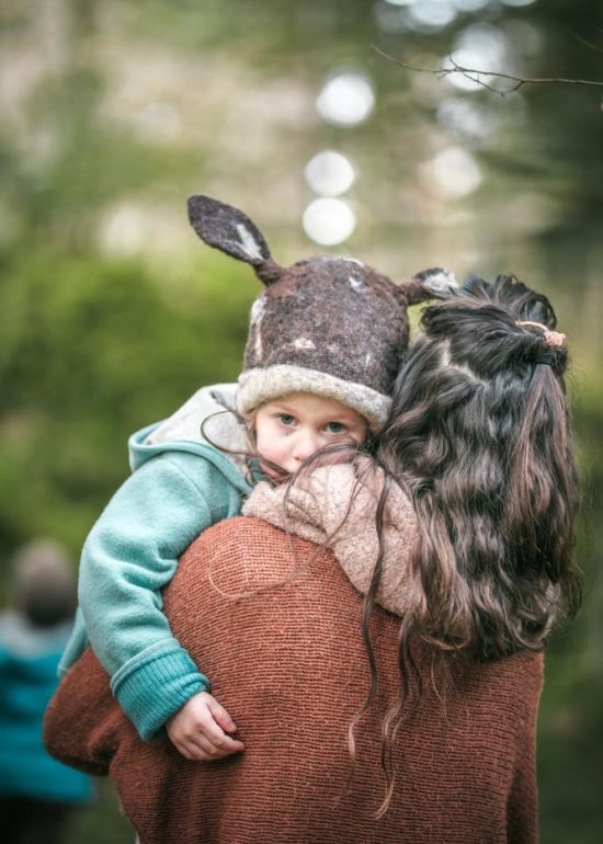 Portrait en plan serré d'une petite fille fatiguée dans les bras de sa maman, elle regarde le photographe par dessus l'épaule de sa mère
