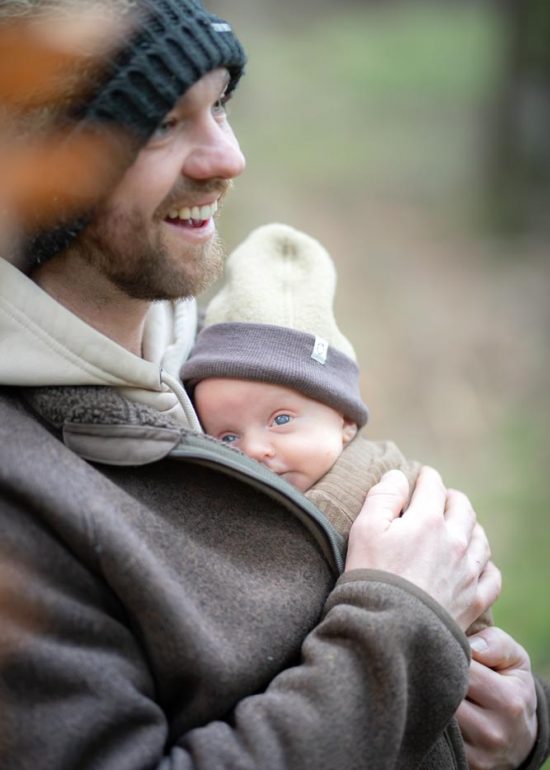 Plan serré sur un bébé les yeux ouverts dans les bras de son papa souriant, en pleine forêt