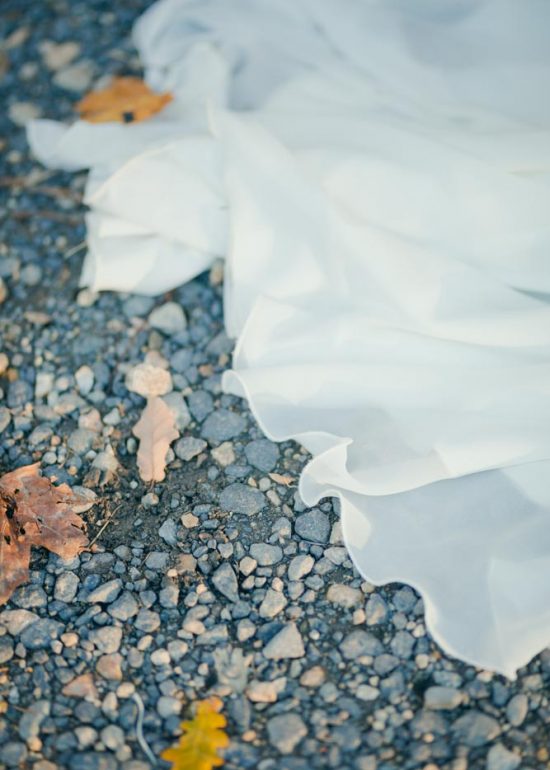 Détails de la robe de mariée traînant sur les graviers d'un parc parsemé de feuilles d'automne