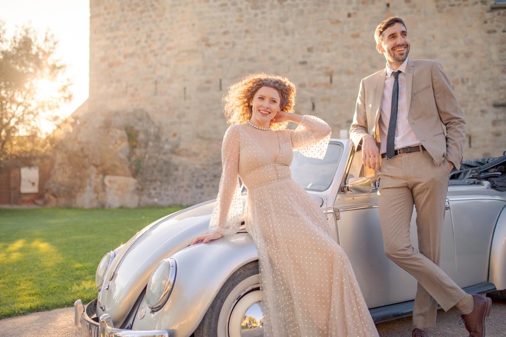 Plan moyen d'un couple appuyé sur une voiture de collection au coucher de soleil, souriant et discutant