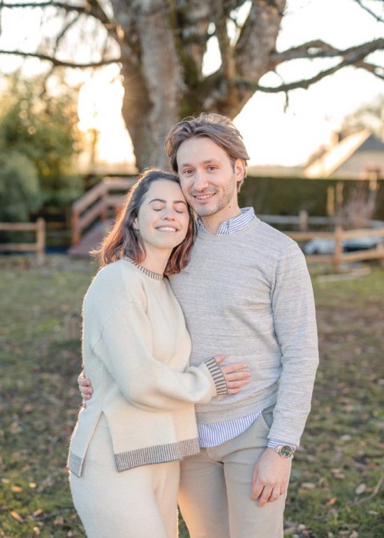 Couple en plan moyen serré l'un contre l'autre dans le jardin familial au coucher de soleil, la femme a la tête posée sur l'épaule de son homme et a les yeux fermé