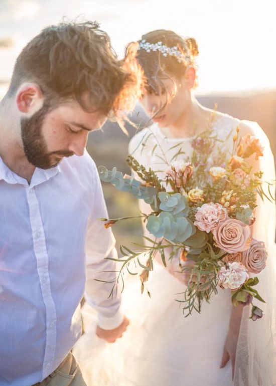 Couple de jeunes mariés, l'homme emmène sa femme qui porte son bouquet pastel, au coucher de soleil