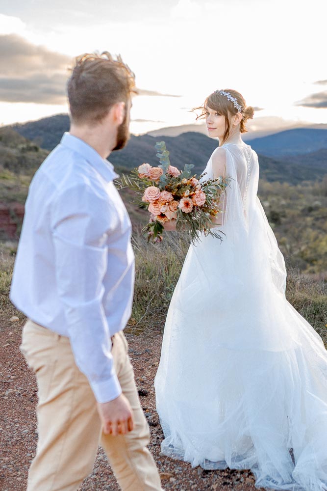 Couple tournant l'un autour de l'autre en montagne au coucher de soleil. La mariée tenant son bouquet est de face et dans le plan de netteté, son mari est devant elle de dos et la regarde