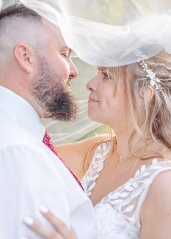 Couple se regardant dans les yeux sous le voile de la mariée recouvrant leurs deux têtes