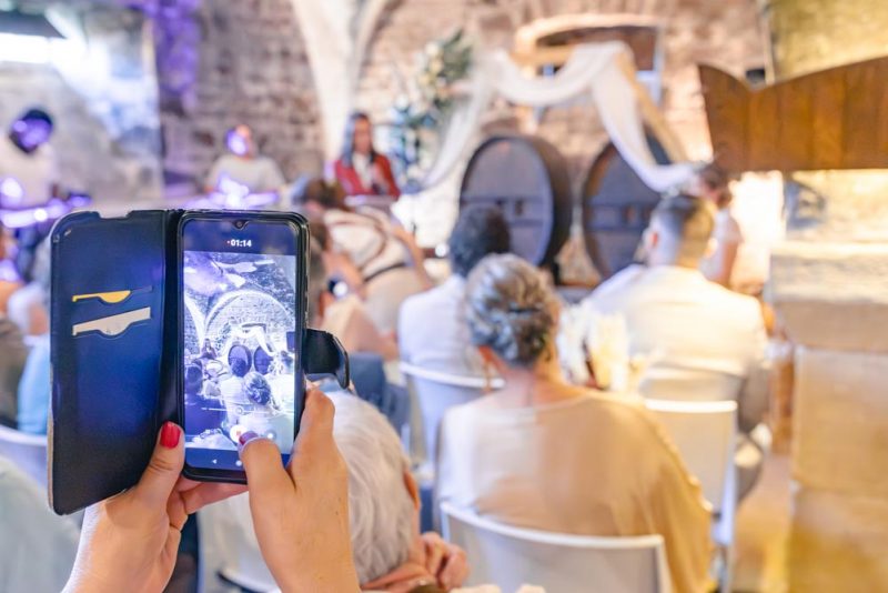Photographie d'un smartphone prenant en photo la cérémonie d'un mariage, l'image visible dans le smartphone étant également visible en arrière plan