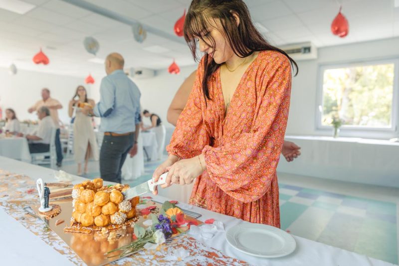 Plan serré de la découpe d'un gâteau de mariage, pièce montée, avec les invités et la table de réception en arrière plan