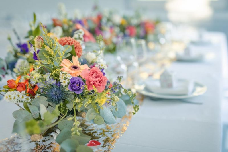 Plan serré sur la composition florale sur la table de réception d'un mariage estival