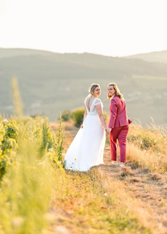 Couple marchant le long d'un champ de vigne au coucher de soleil et se retournant vers le photographe