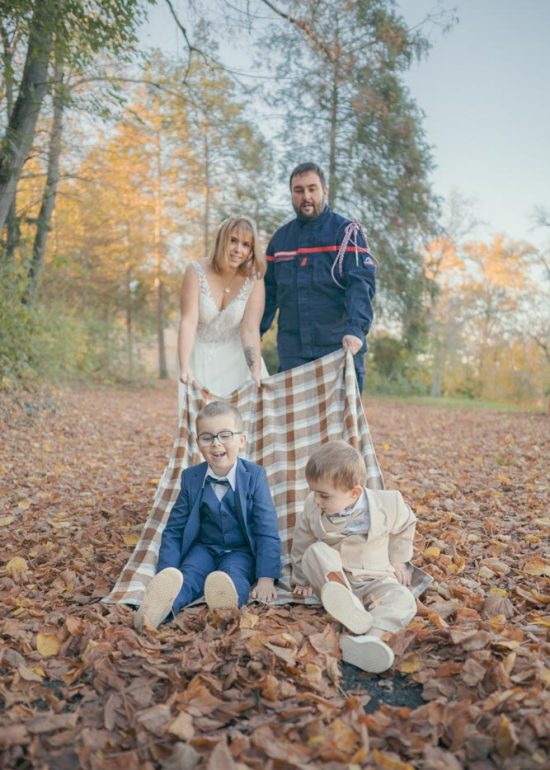 Couple debout et riant tirent une couverture sur laquelle sont assis leurs deux enfants, qui rient d'être trainées dans les feuilles mortes