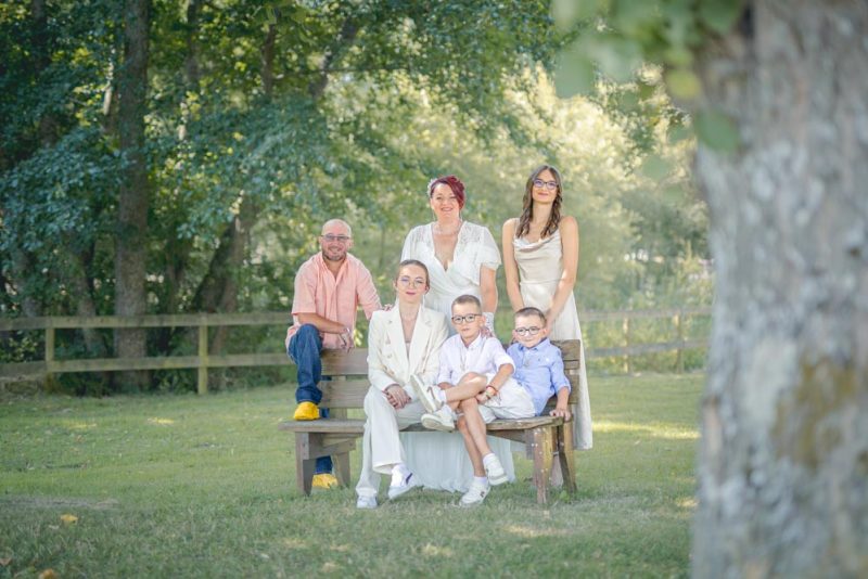 Photographie en plan large d'un famille assise sur un banc dans un parc verdoyant