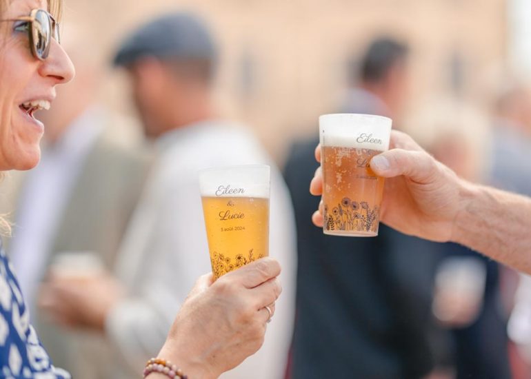 Invités trinquant lors de la réception avec deux éco-cups signés des noms des mariées et de la date
