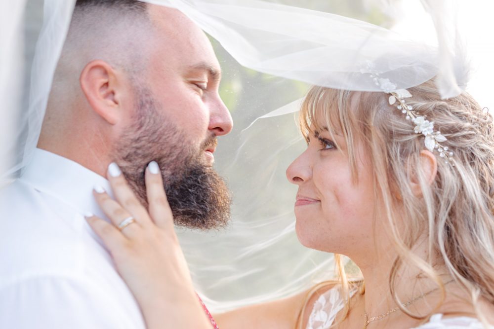 Couple se regardant dans les yeux sous le voile de la mariée recouvrant leurs deux têtes